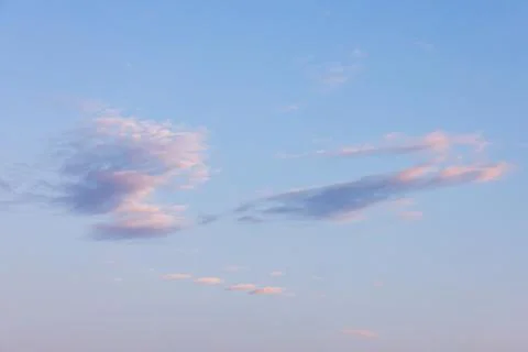 Soft pastel clouds float across a pale blue sky at sunset Foto stock