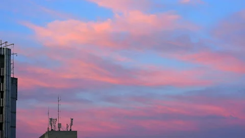 Soft pink and blue clouds spreading across the evening sky above urban buildings Stock Footage 336940152