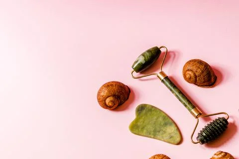 Soft pink background with seashells and jade facial massagers. Stock Photos