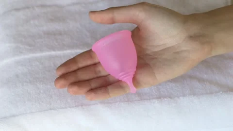 Soft pink menstrual cup standing on open palm with flower in background. Gentle Stock Footage 330460122