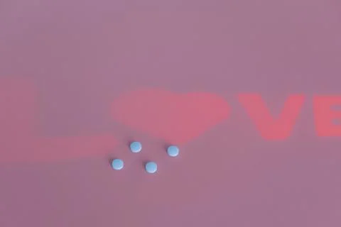 Soft pink surface holds four light blue pills implying oral medication used t Stock Photos