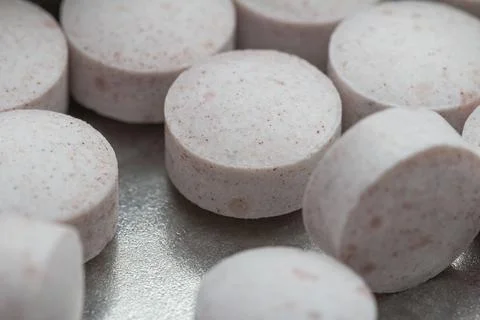 Soft pink tablets rest on a metallic surface Stock Photos