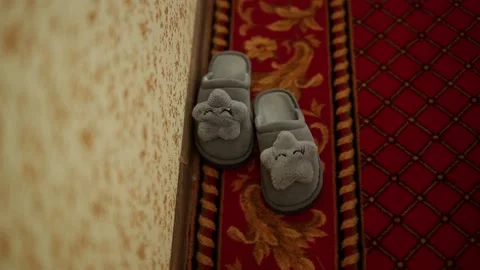 Soft plush gray slippers with a star stand on an expensive carpet near the wall Video stock 153616991
