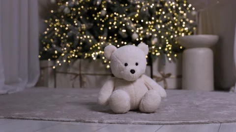 Soft plush teddy bear sitting on carpet with Christmas tree lights in background Stock Footage 323224206