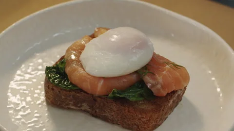 Soft poached egg benedict with smoked salmon on crispy spinach brioche toast 스톡 동영상 150963612