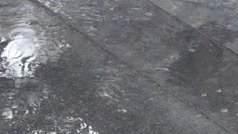 Soft rain falls on black tiled entrance steps. Gentle ripples dance on the gloss Stock Footage 338313989