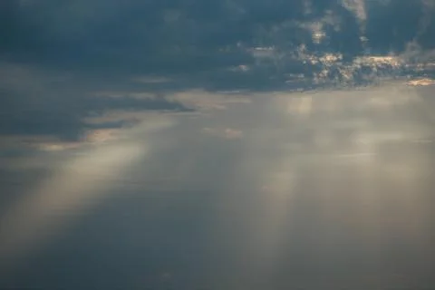Soft rays of sunlight break through dark clouds in a dramatic sky, creating.. Stock Photos