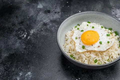 Soft rice and crisp edged fried egg in a rustic bowl photographed on dark t.. Stock Photos