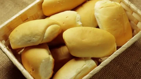 Soft rolls arranged in a rustic straw basket on natural jute fabric Видео 337210209