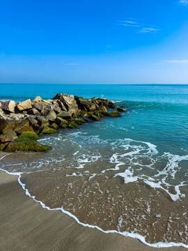 Soft sandy beach meets tranquil ocean waves as they gently kiss the rocky jet 写真素材