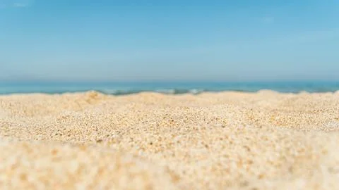 Soft sandy beach texture meets blurred turquoise sea horizon under clear sky, Stock Photos