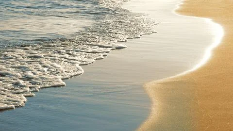 Soft sea waves rushing on sandy beach at sunset Stock Photos