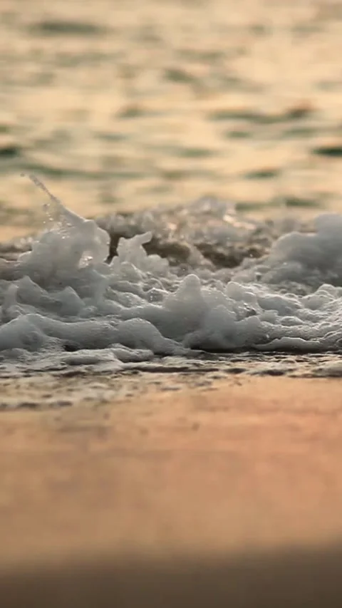 Soft sea waves with white foam washing over a sandy beach during golden sunset 库存影片 329181542
