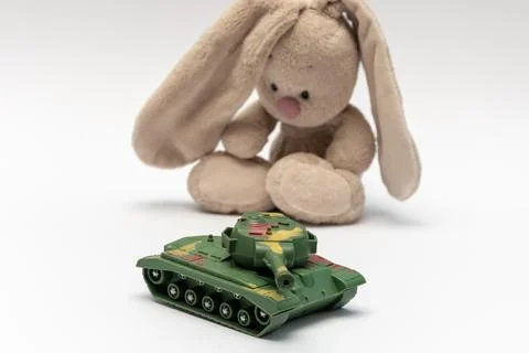 Soft stuffed bunny sits behind green toy tank isolated on white Stock Photos