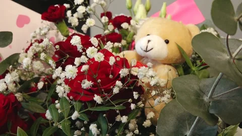 A soft teddy bear nestled among vibrant red roses, white baby's breath, and Видео 331039003