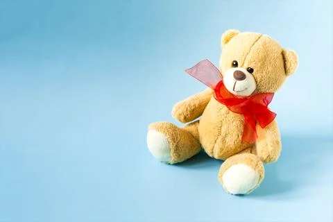 A soft teddy bear with a red bow on a light background. Stock Photos