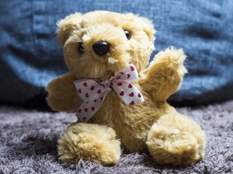 Soft toy fluffy bear with a bow around his neck sits on the carpet Stock Photos