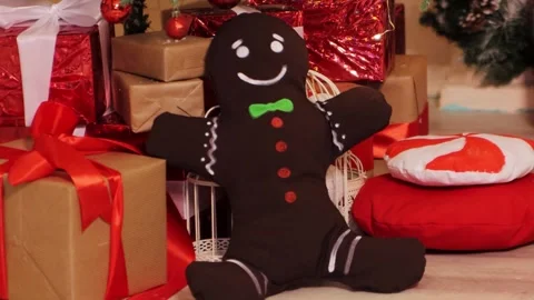 A soft toy gingerbread man sits on a background of Christmas gifts Stock Footage 252876103