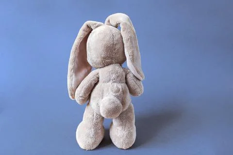 Soft toy hare stands facing away on a bright blue background Stock Photos