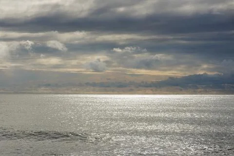Soft view of the sun behind the rainy clouds over the calm sea Stock Photos
