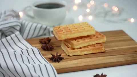 Soft waffles falling down on a wooden board next to strings of light. Video stock 168120762