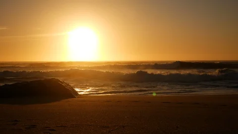 Soft, warm light with lens flare on beach at sunset. Rock on shoreline Stock Footage 104683088