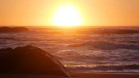 Soft, warm light at sunset on beach looking over ocean with rock in foreground Stock Footage 104684488
