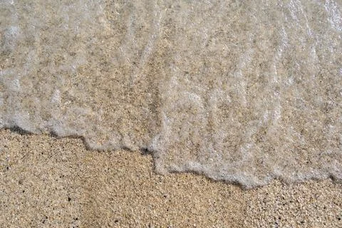 A soft wave runs on a sandy shore on a summer day. Stock Photos