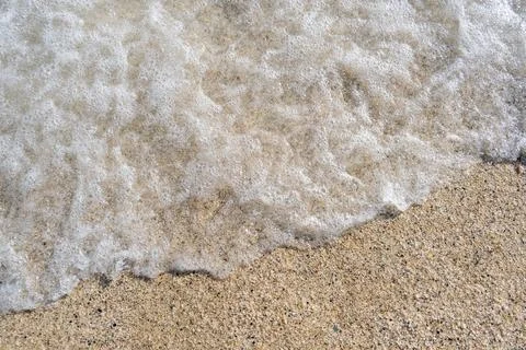 A soft wave runs on a sandy shore on a summer day. Stock Photos