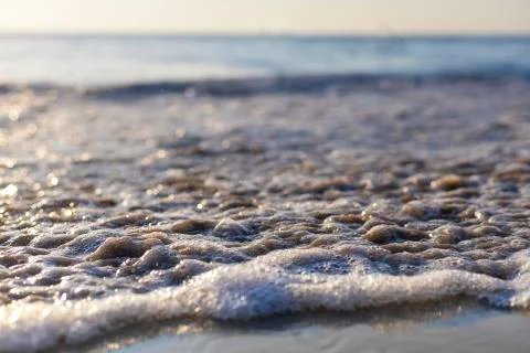 Soft wave from sea come to wet sand beach with blur clear sky background. Wit Stock Photos