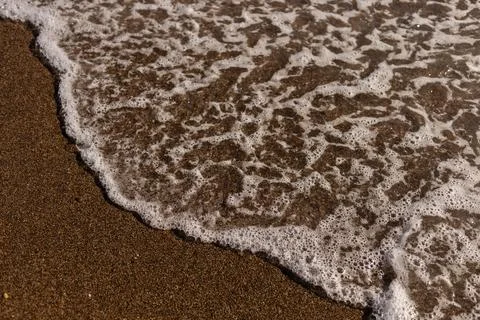 Soft waves are lapping against the golden sand on a beach during a bright day Stock Photos