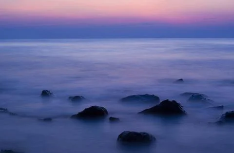 Soft waves on a rocky beach in the evening Stock Photos