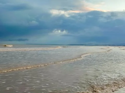 Soft waves roll onto the beach as dark clouds gather over the horizon in th.. Fotos Stock