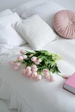Soft white bedding adorned with decorative pillows and a bouquet of pink tulips Stock Photos