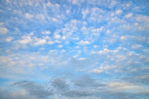 Soft, white clouds drift across a clear blue sky Stock Photos