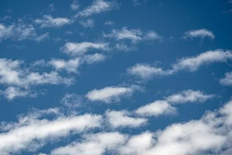 Soft white clouds scattered across a vivid blue sky in sunny weather Stock Photos