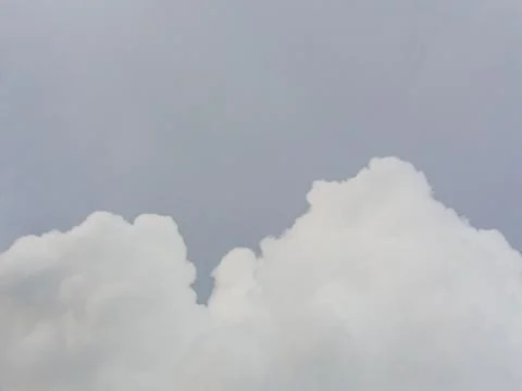 Soft white cumulus clouds rising under a gray overcast sky create a calm Foto stock