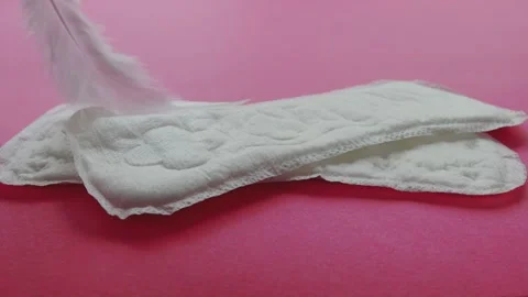 A soft white feather traces over feminine sanitary pads on a pink background Stock-Footage 255634716