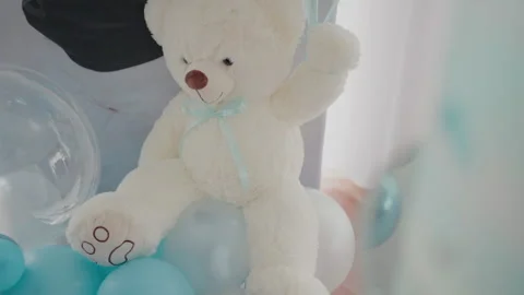 Soft white teddy bear with a blue ribbon sitting among blue and clear Stock Footage 278656218