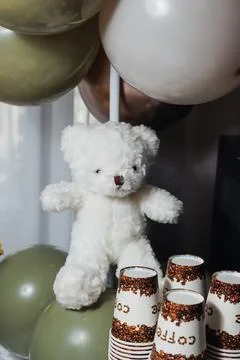 Soft white teddy bear sits beside festive balloons Foto stock