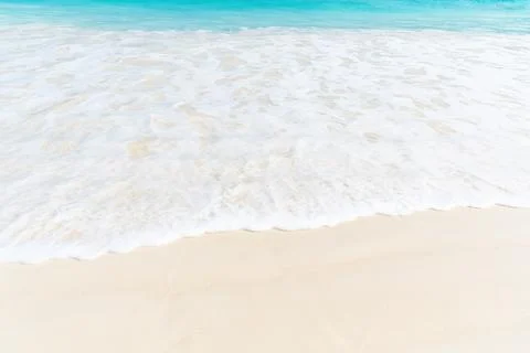 A soft, white wave gently laps onto the sandy beach, creating a calming scene Stock Photos