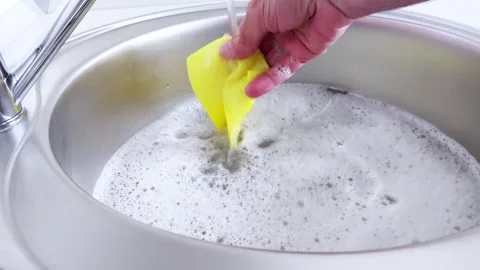 Soft Yellow Sponge Swirls Through Soapy Water in a Silver Sink Video stock 313520863
