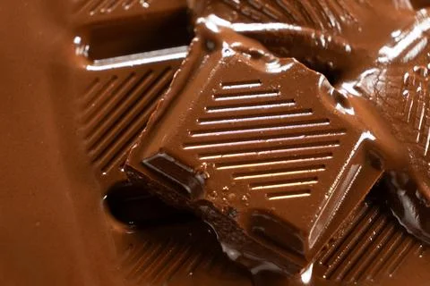 Softened chocolate bar squares dissolving into warm liquid chocolate pool Stock Photos