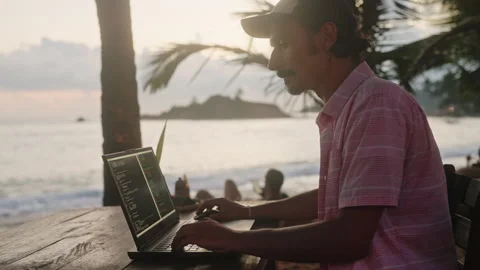 Software dev works on laptop at beachside cafe. Man writes code during ocean Stock Footage 280492865