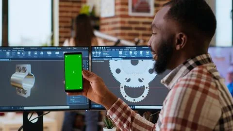 Software developer creates a gear prototype on dual monitors next to chroma key Stock Photos