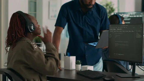 Software developer holding laptop and talking to programer at desk Stock Footage 220894913