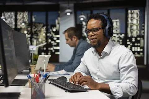Software developer listening music in office, reviewing system metrics Foto stock
