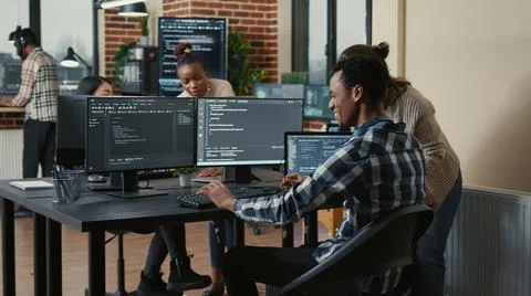 Software developer looking at running code on multiple screens takes off glasses Stock Photos