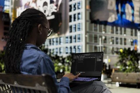 Software developer on park bench writes code on laptop Stockfoto's
