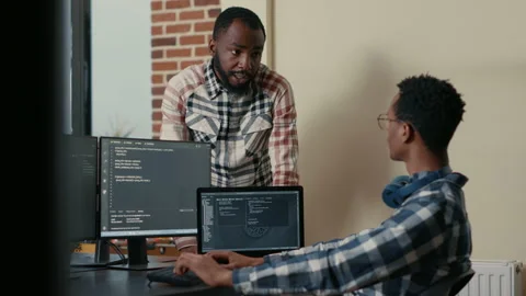 Software developer sitting at desk with multiple screens and laptop running code Stock Footage 168245535